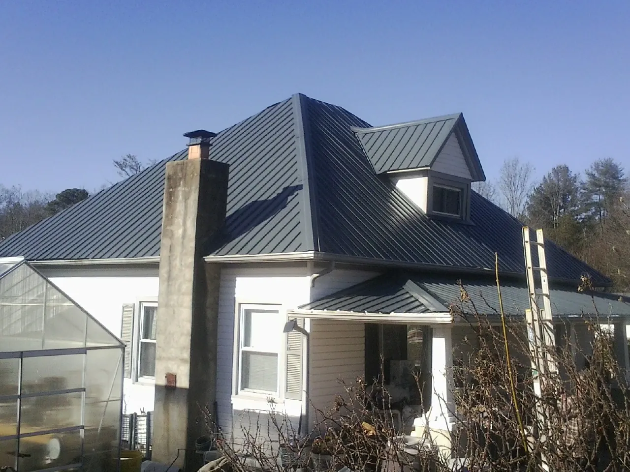 Dark blue standing seam metal roof on a white farmhouse with dormer — Slate & Tile Roof Repair by Roofing Brothers in Skillman