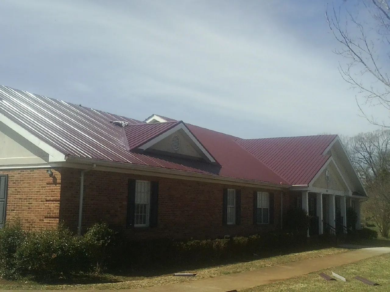 Red metal roof with gabled entries on a long brick building, from a Hail Damage Roof Repair job in Skillman