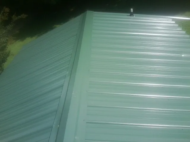 New green metal panels meeting at the ridge of a roof — Flat Roof Repair work by our crew in Skillman