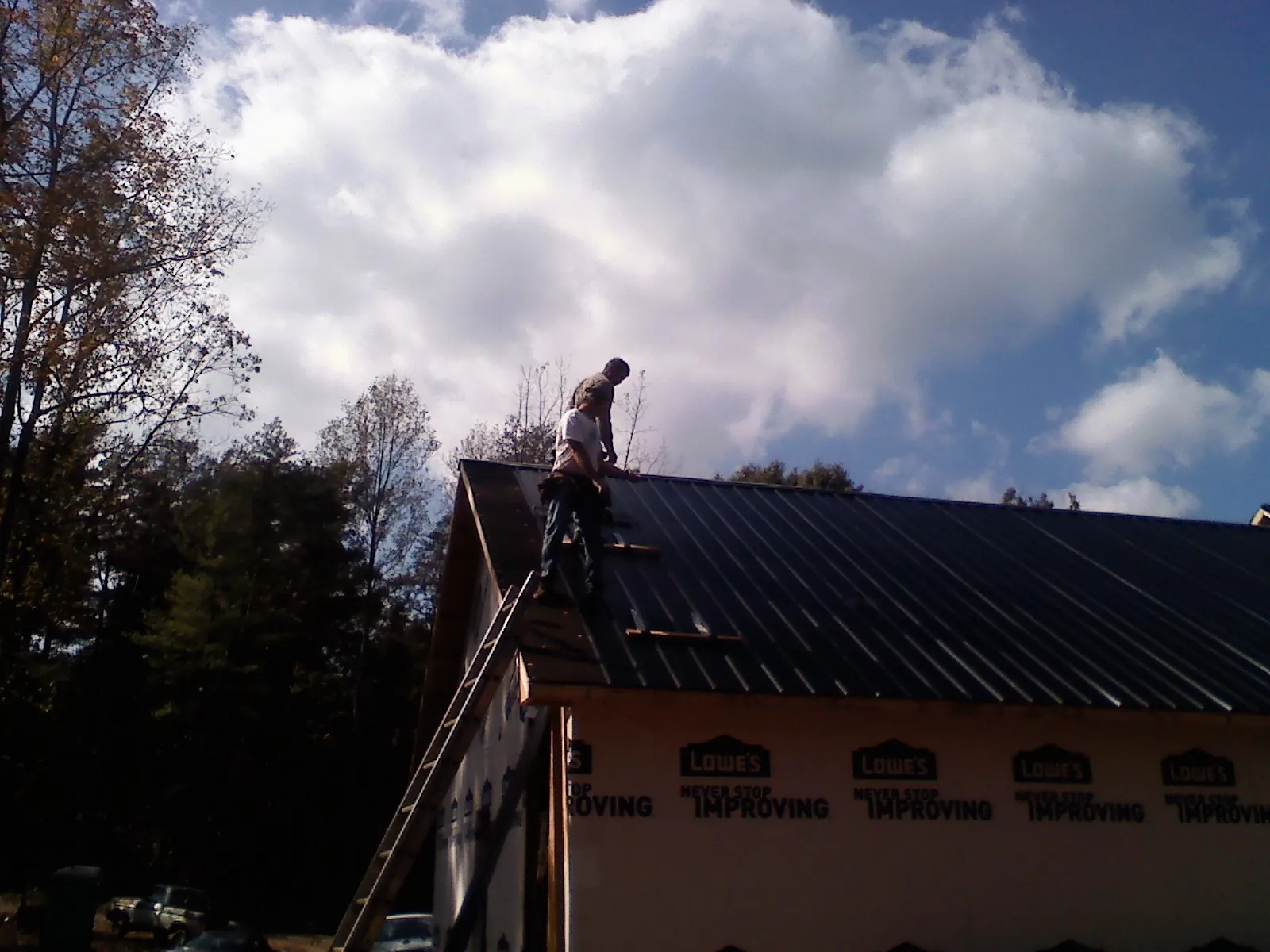 Roofer fastening dark metal panels high against a cloudy sky, from a Roof Inspection job in Skillman