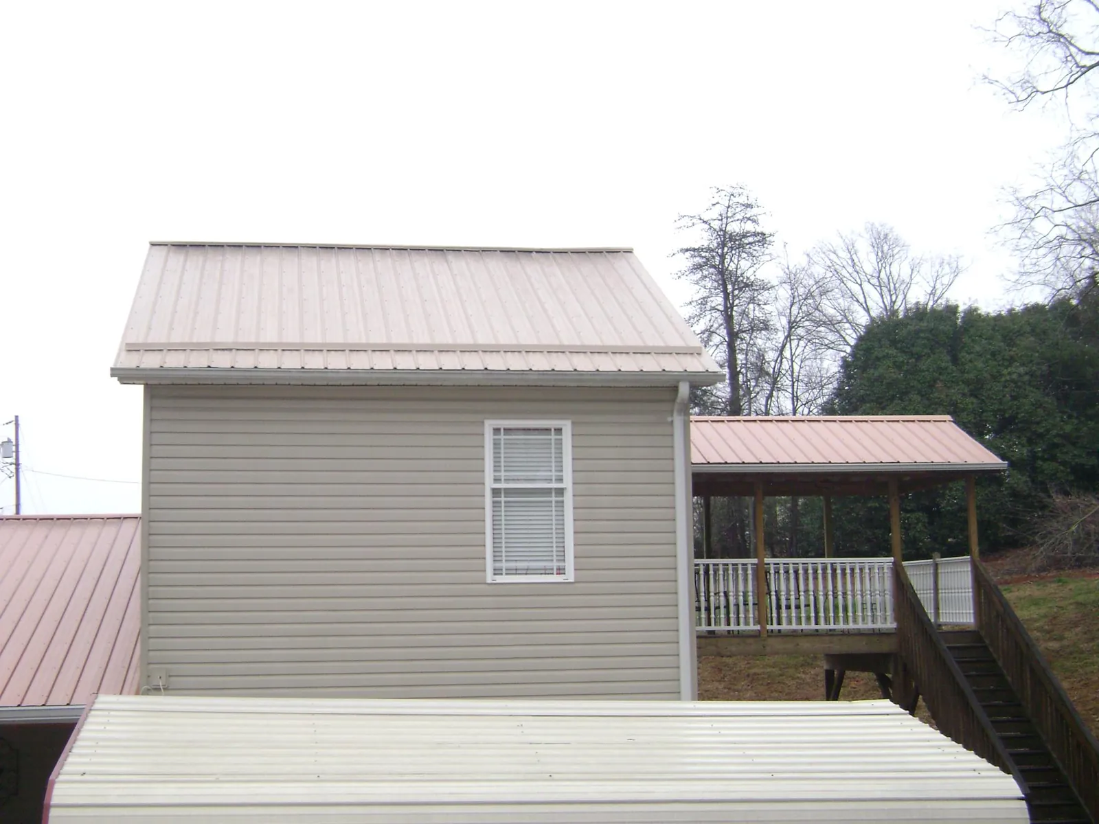 Tan metal roofs on a two story addition and attached porch, from a Roof Replacement job in Skillman